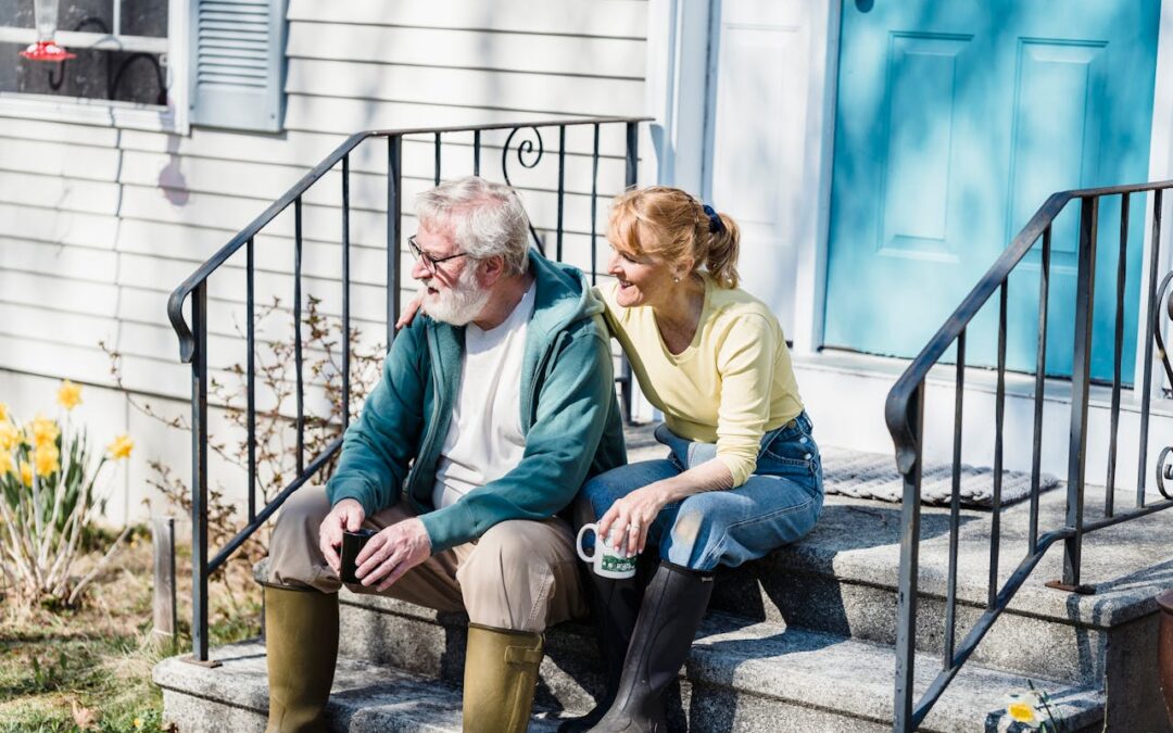 Middle aged lady with arm around older gentleman, possibly her father. Sitting on steps of house and smiling.